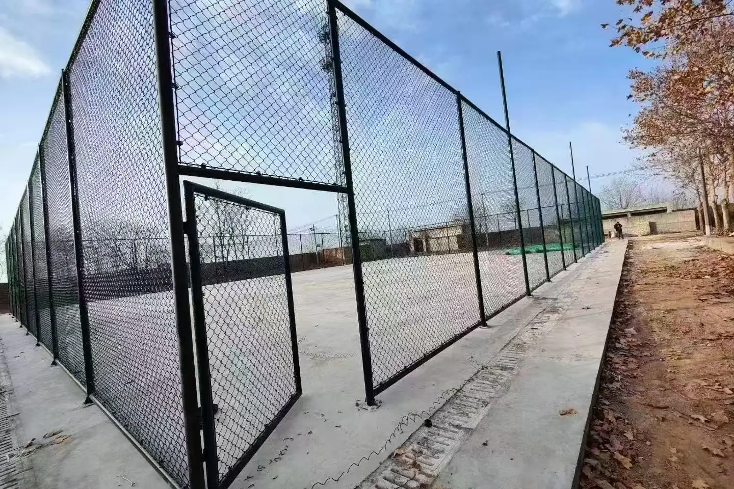 Green sports fence with a matching access gate beside a blue court
